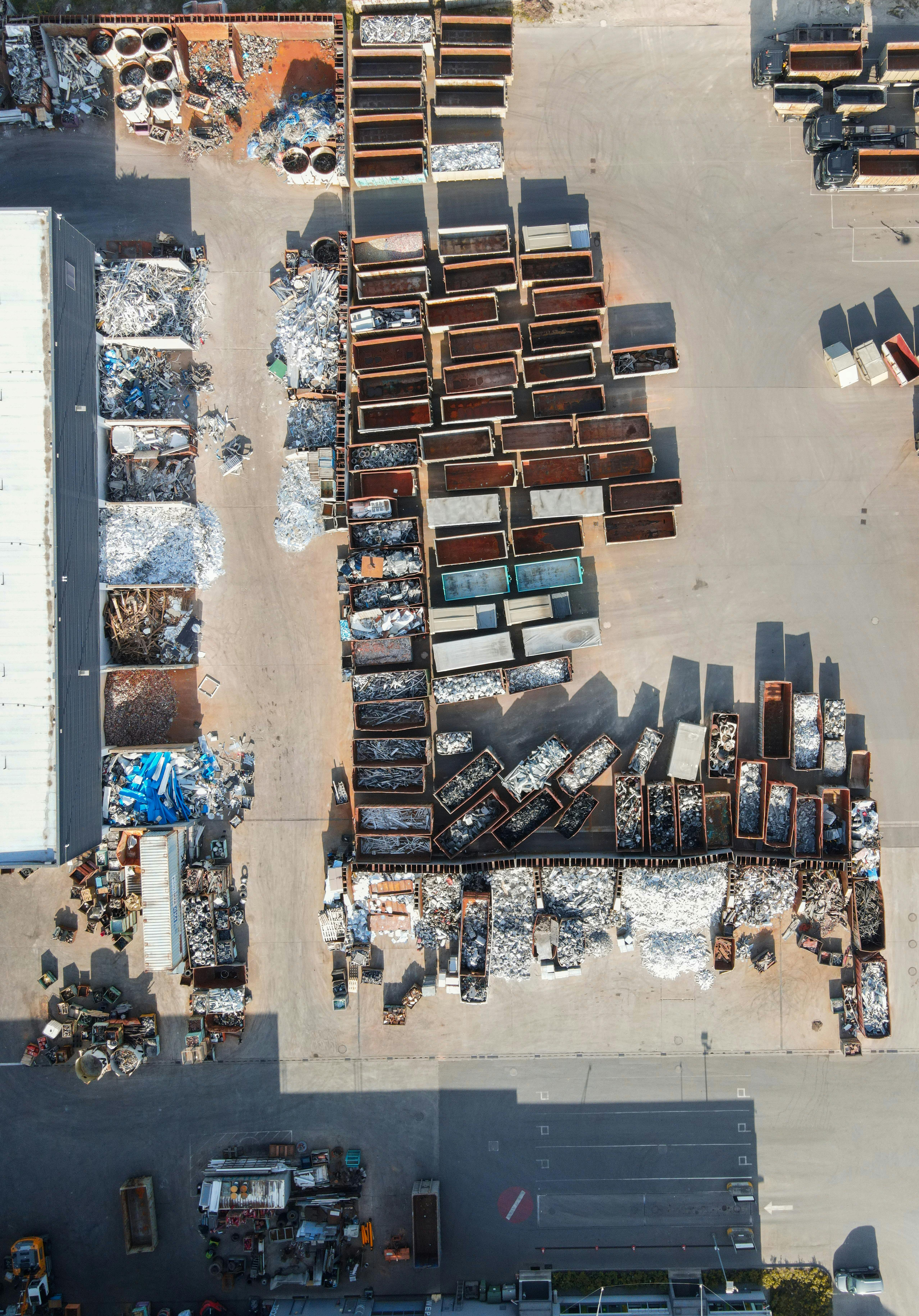 Imagem aérea de um pátio industrial com diversos contêineres organizados em fileiras, contendo diferentes tipos de sucata metálica e materiais recicláveis, prontos para triagem, reaproveitamento ou destinação adequada.