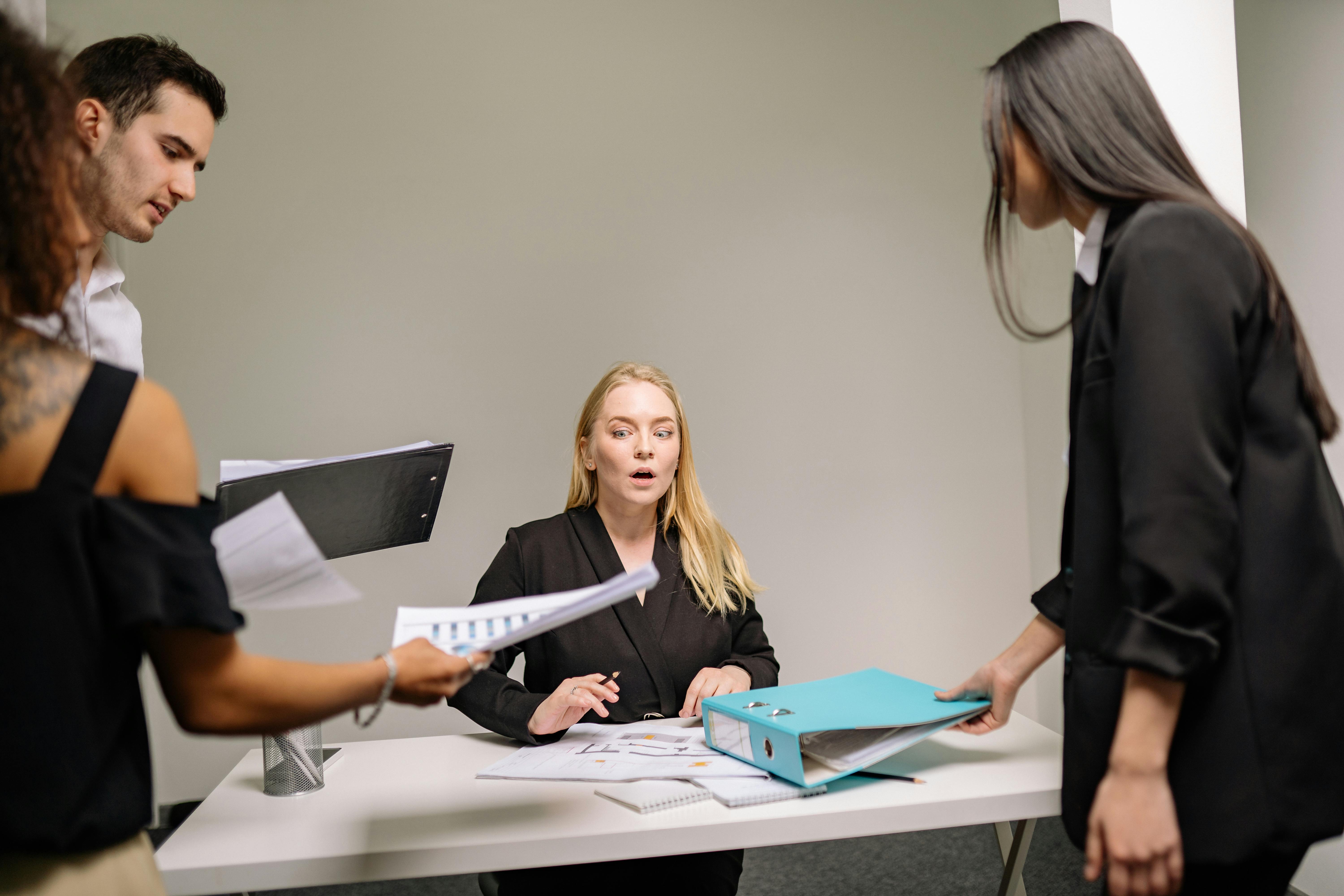 Mulher loira em ambiente de trabalho apreensiva ao receber algumas pastas com demandas